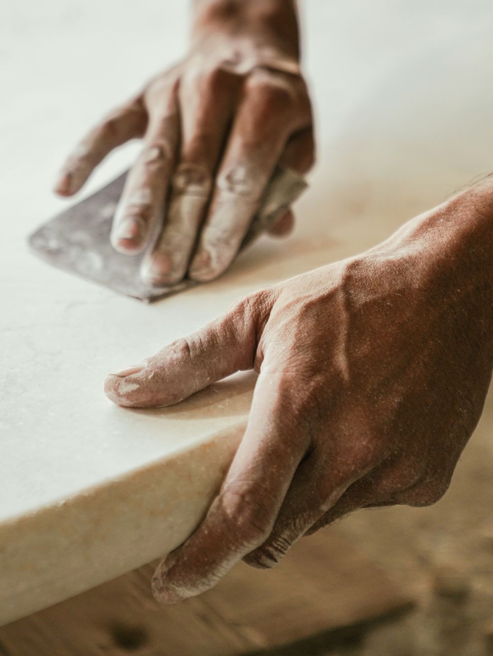 Craftsperson sanding a stone surface by hand, carefully finishing its edge
